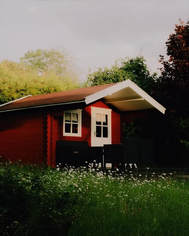 A red wooden cabin in a summer garden with the Astia look