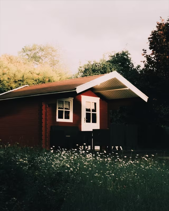 A red wooden cabin in a summer garden with the Bark Morken look
