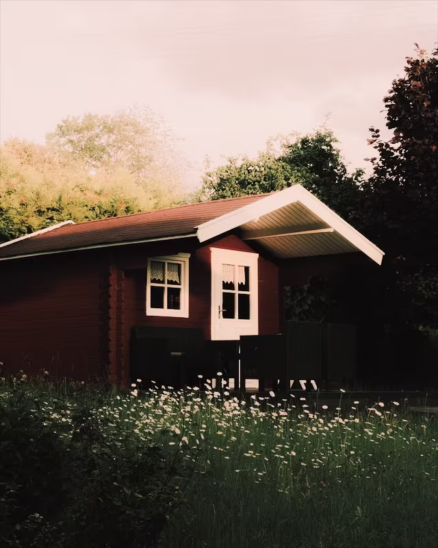 A red wooden cabin in a summer garden with the Classic Cuban look
