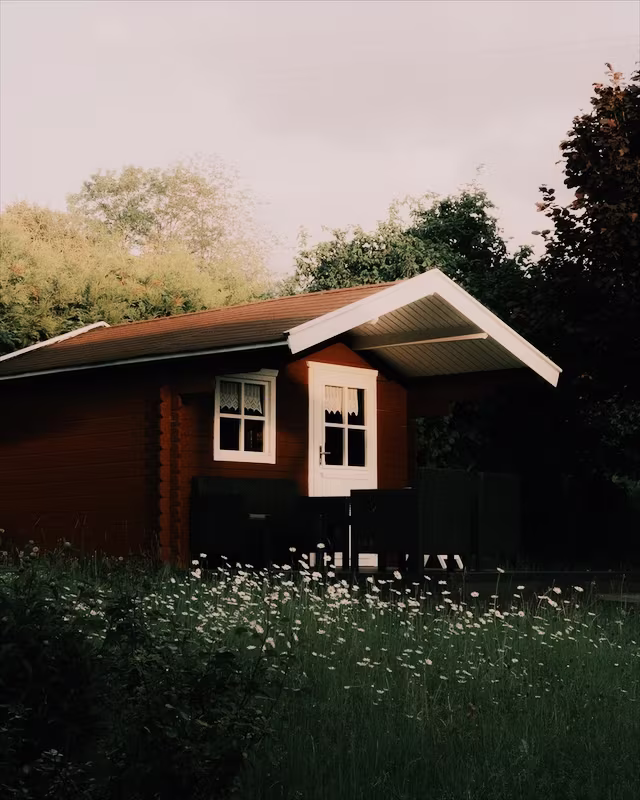 A red wooden cabin in a summer garden with the Classic Neg look
