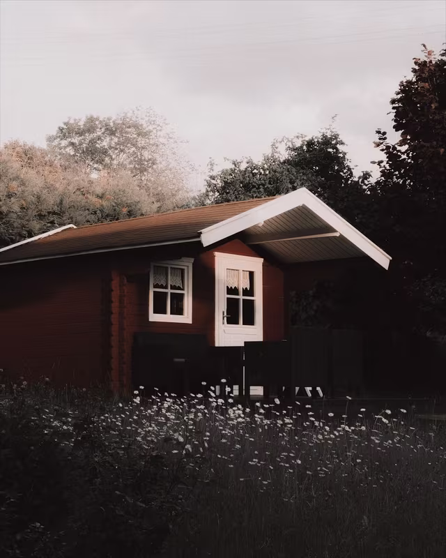 A red wooden cabin in a summer garden with the Coffee look