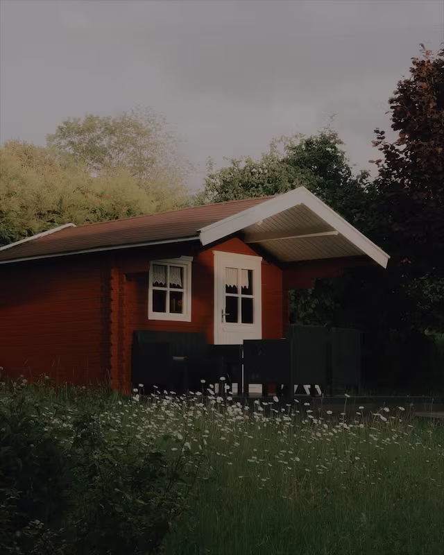 A red wooden cabin in a summer garden with the Eterna look