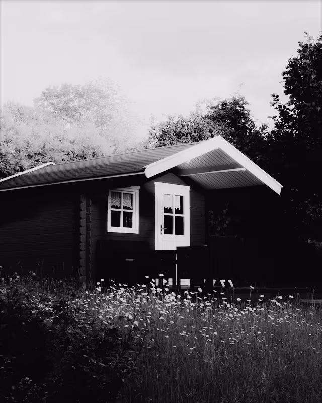 A red wooden cabin in a summer garden with the Ilford Delta look