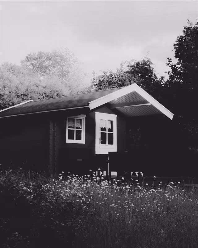 A red wooden cabin in a summer garden with the Ilford Delta Faded look