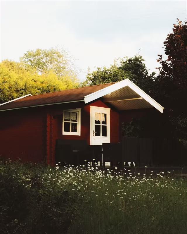 A red wooden cabin in a summer garden with the Kodak Gold look