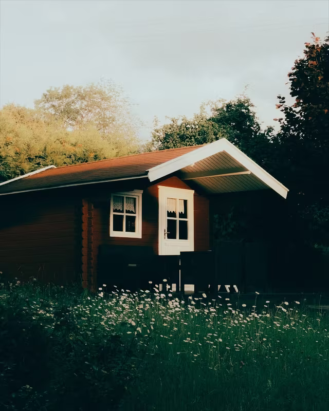 A red wooden cabin in a summer garden with the London look