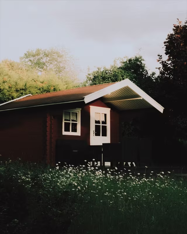 A red wooden cabin in a summer garden with the Portra 400 look