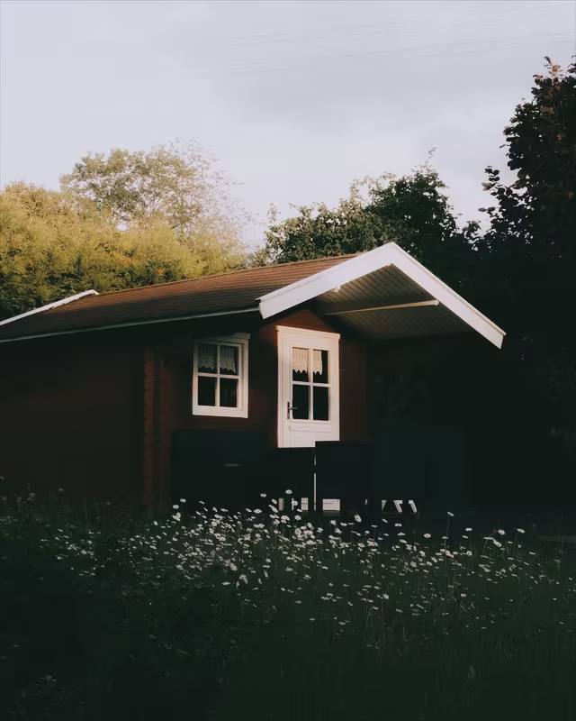 A red wooden cabin in a summer garden with the Polaroid look