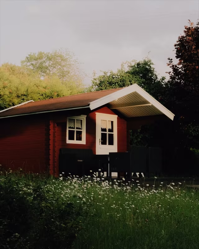 A red wooden cabin in a summer garden with the Provia look