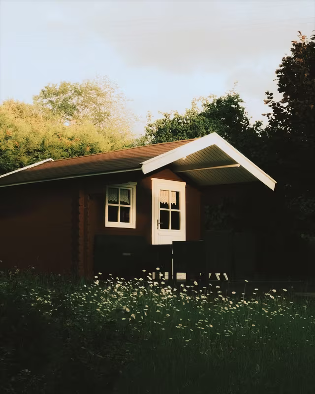 A red wooden cabin in a summer garden with the Summer Glow look