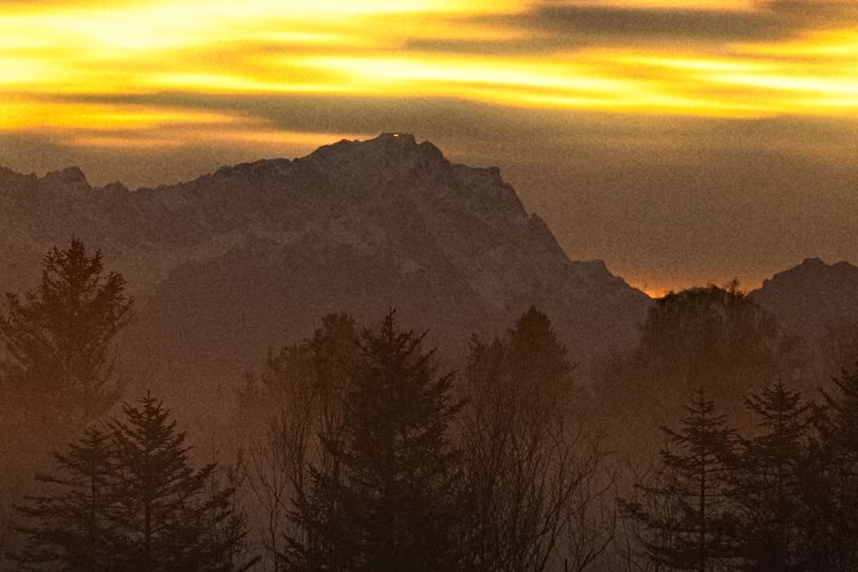 A section of a sunset over misty mountains and pine trees at full size, with film grain added